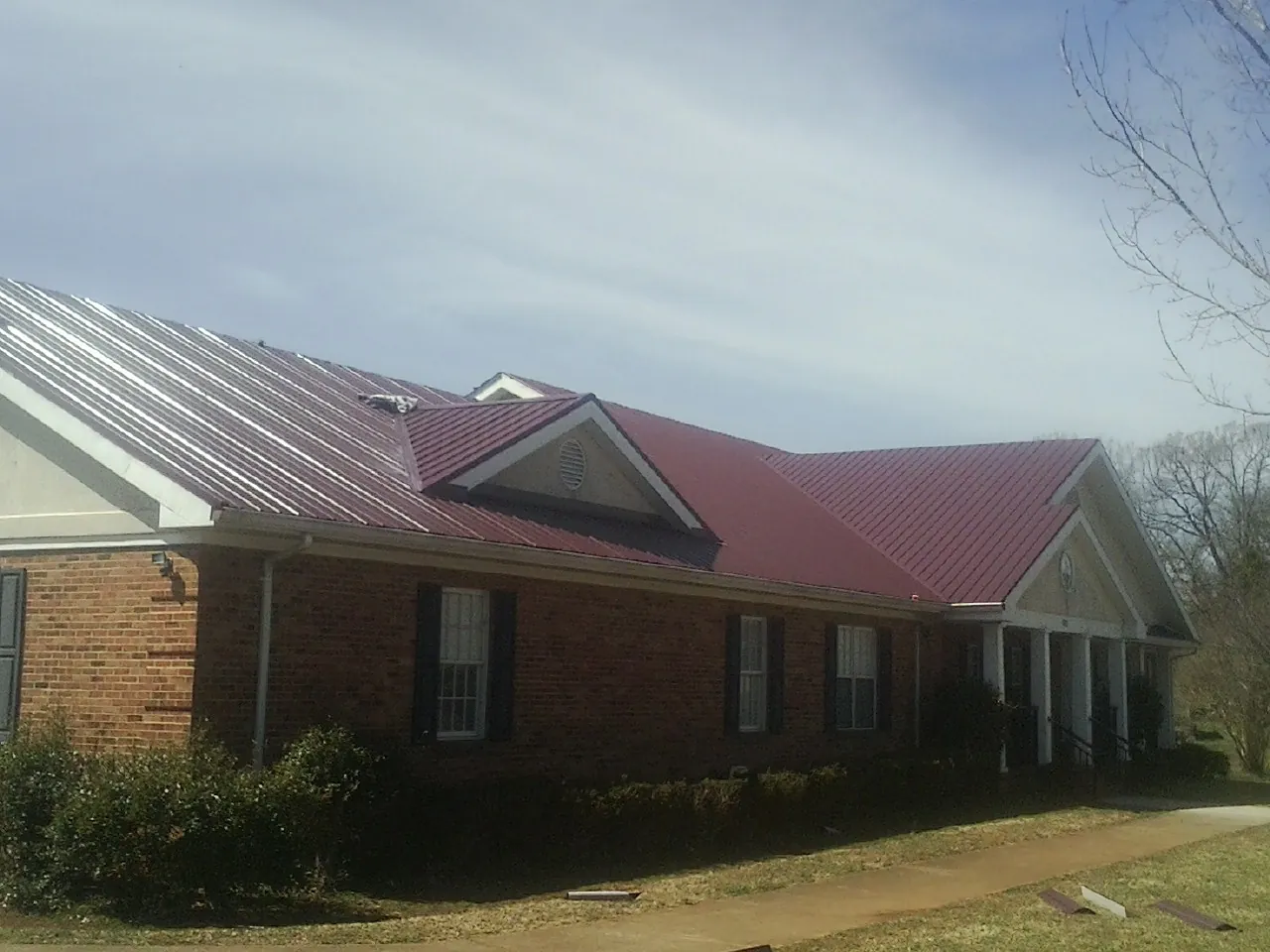 Red metal roof with gabled entries on a long brick building, from a Hail Damage Roof Repair job in O Fallon