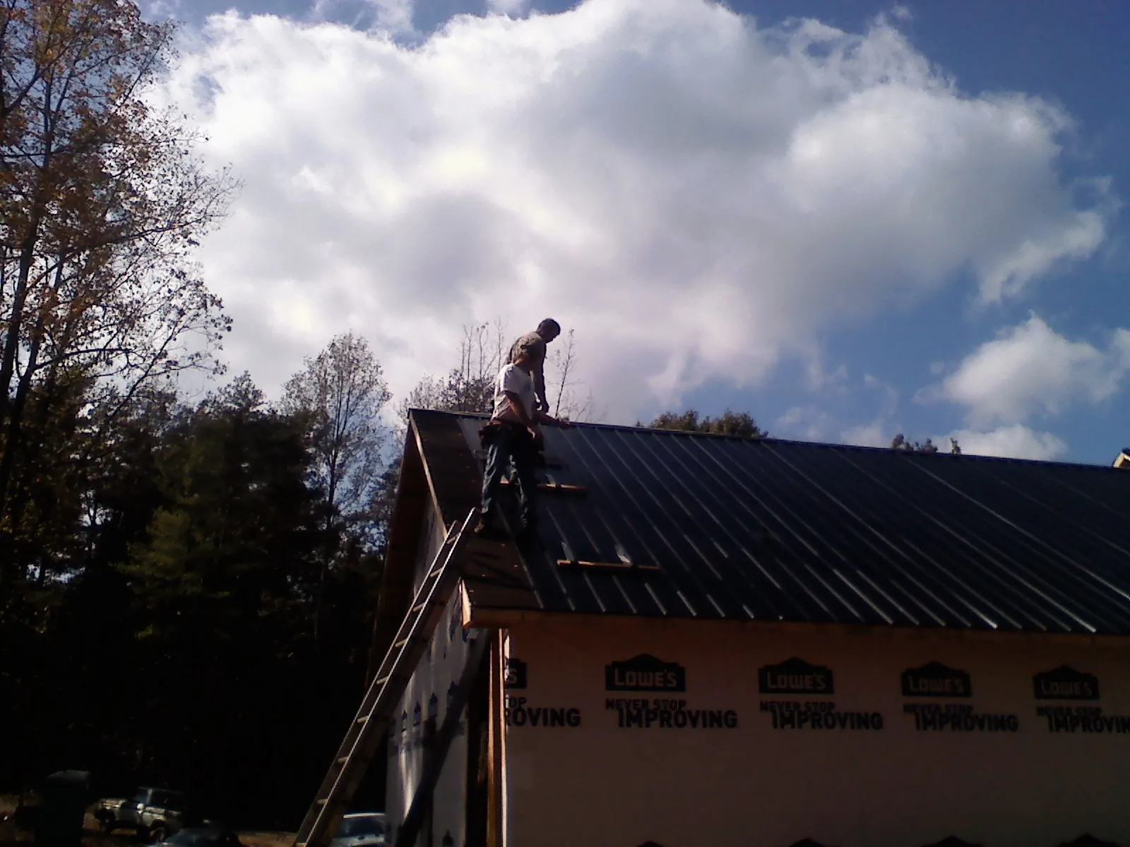 Roofer fastening dark metal panels high against a cloudy sky, from a Roof Inspection job in O Fallon
