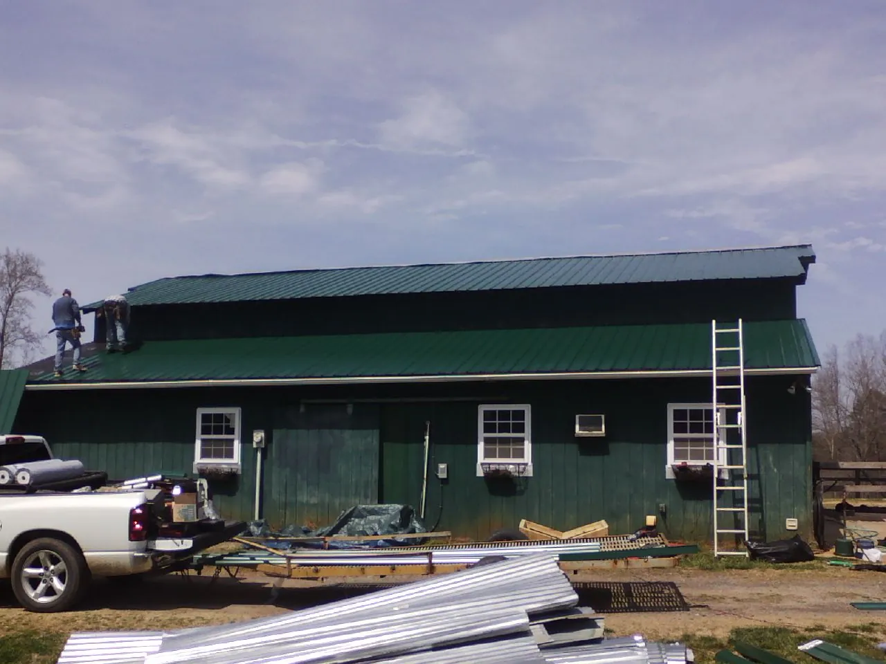 Crew installing green metal roofing on a large green barn in O Fallon